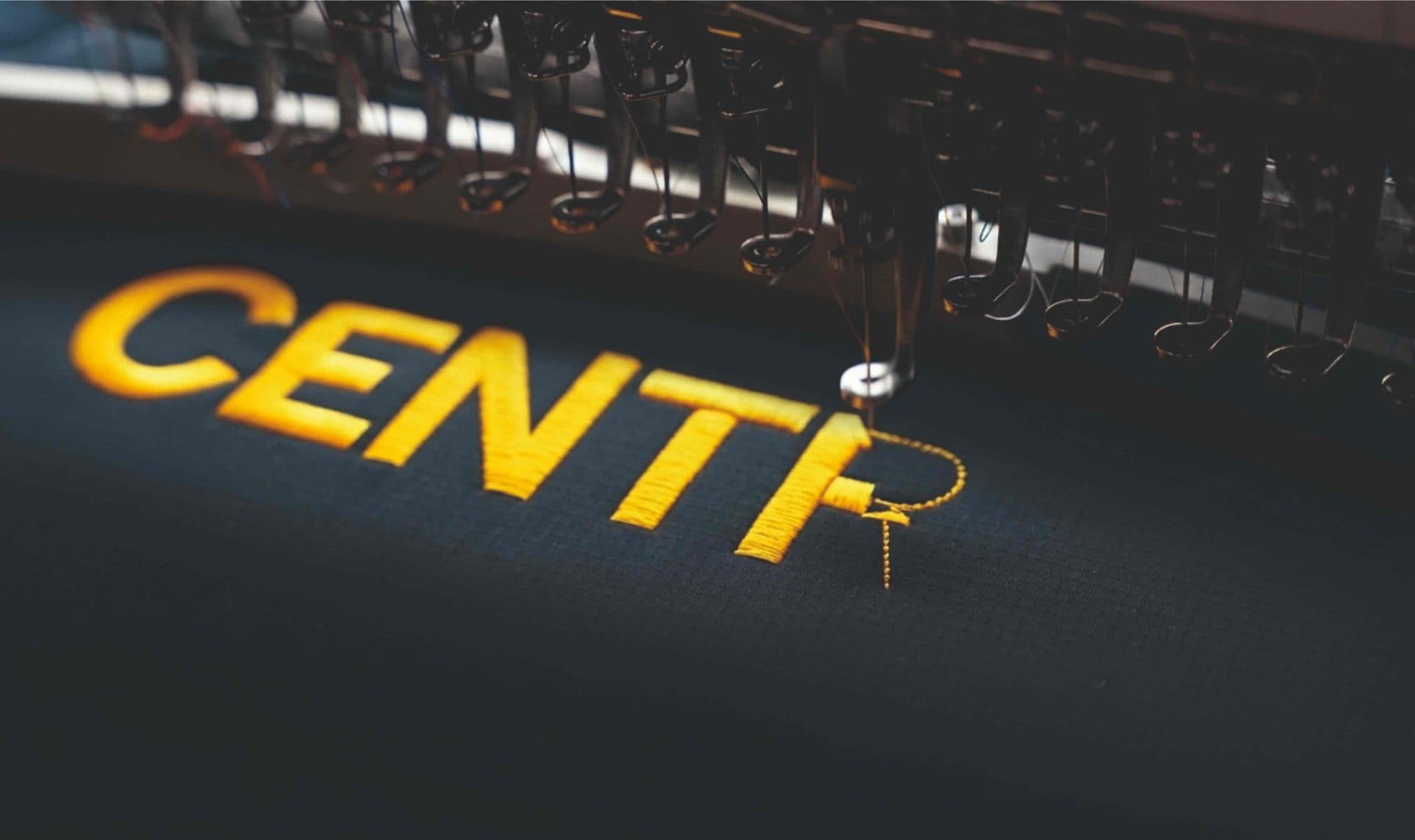 A multi head embroidery machine stitching a yellow logo onto navy fabric